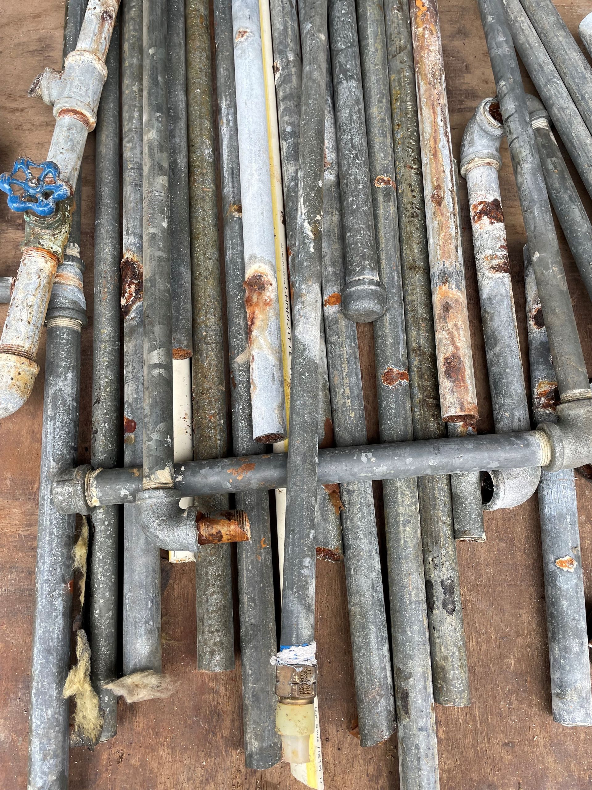A bunch of rusty pipes are stacked on top of each other on the ground.