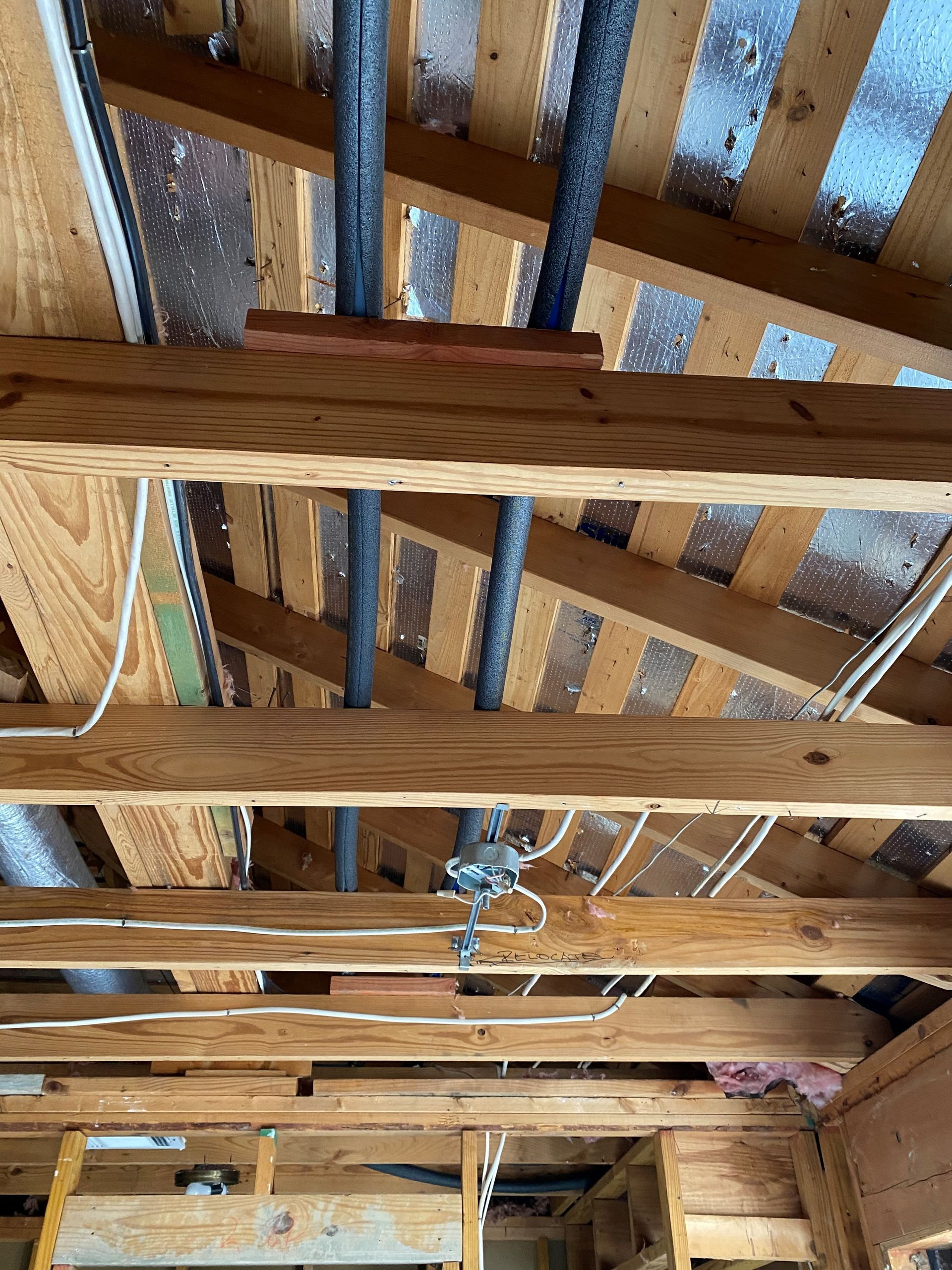 The ceiling of a house under construction with wooden beams and pipes.