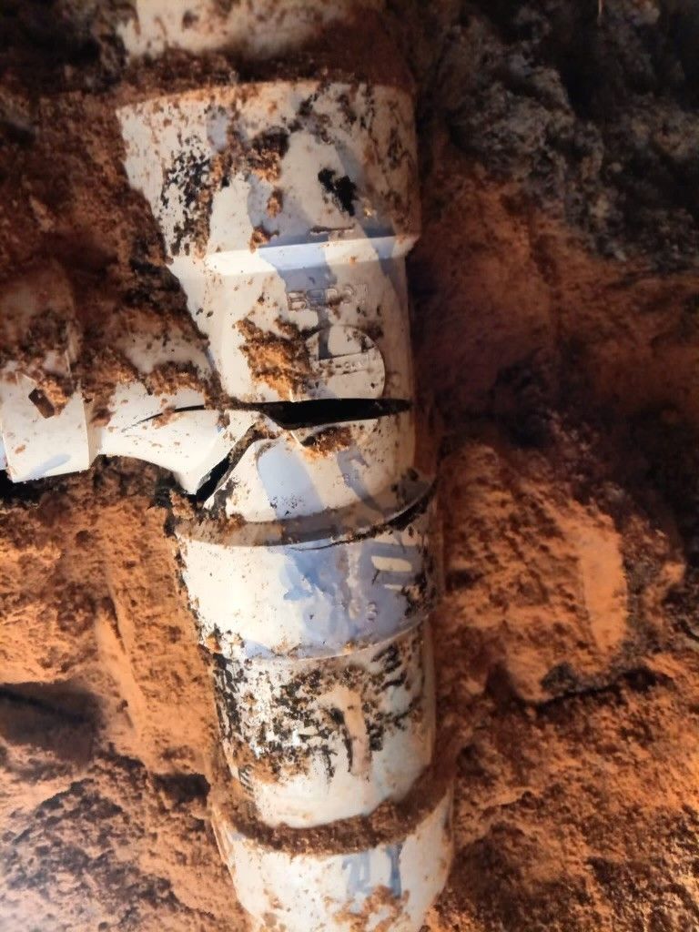 A close up of a broken drain pipe in the dirt.