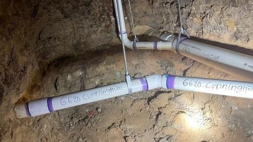 A bunch of pipes are hanging from the ceiling in a basement.