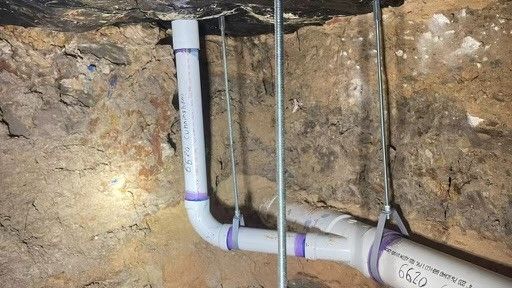 A bunch of pipes are hanging from the ceiling in a basement.