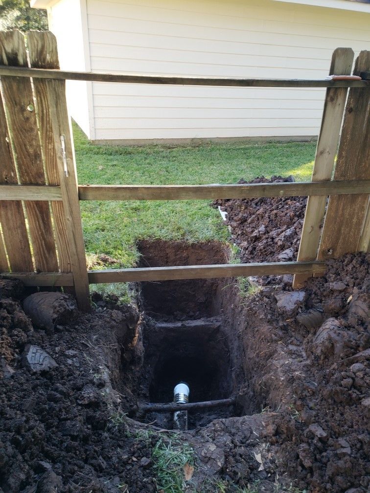 A wooden fence is surrounding a hole in the ground in front of a house.