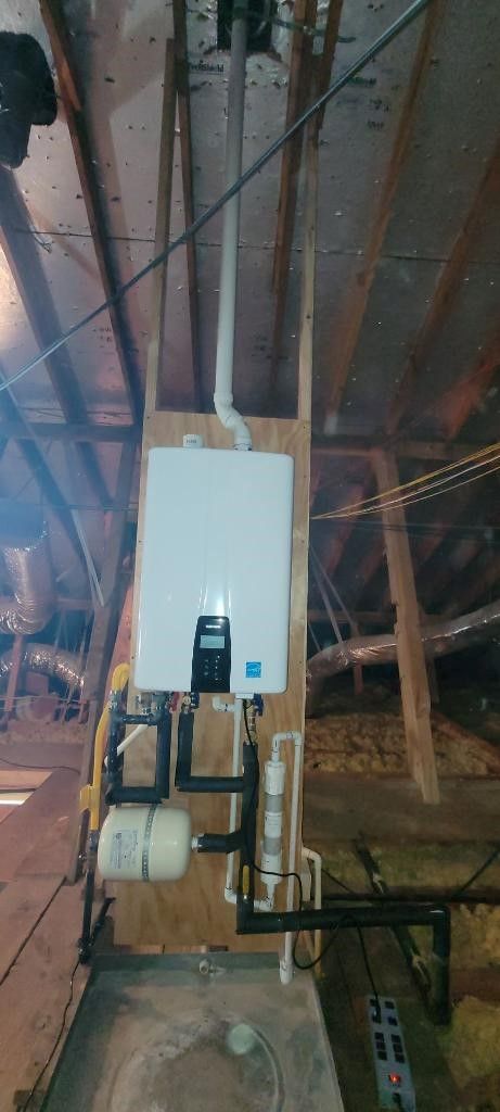 A white water heater is hanging from the ceiling of an attic.