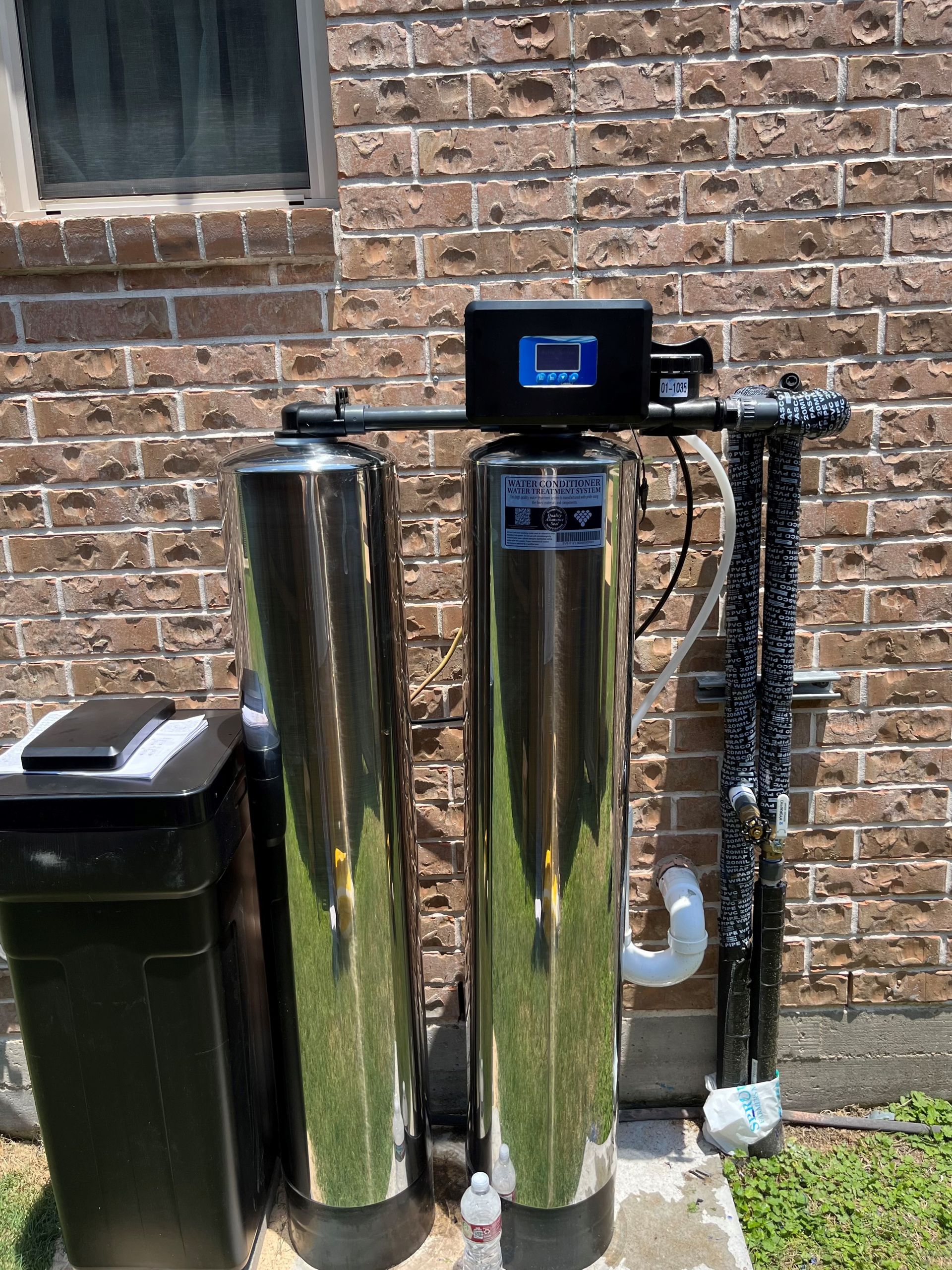 Two stainless steel water filters are sitting in front of a brick building.