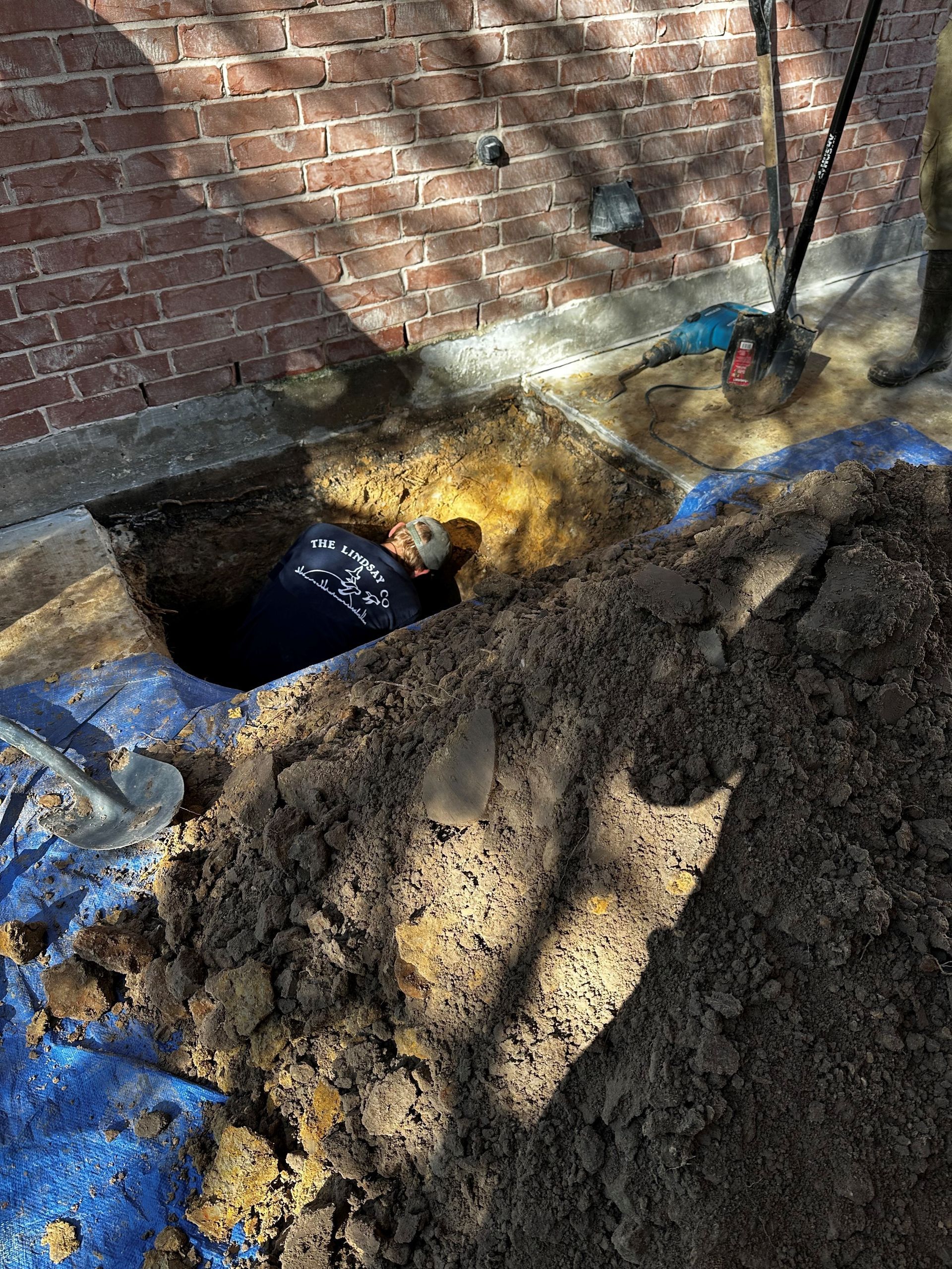 A man is digging a hole in the ground next to a brick wall.