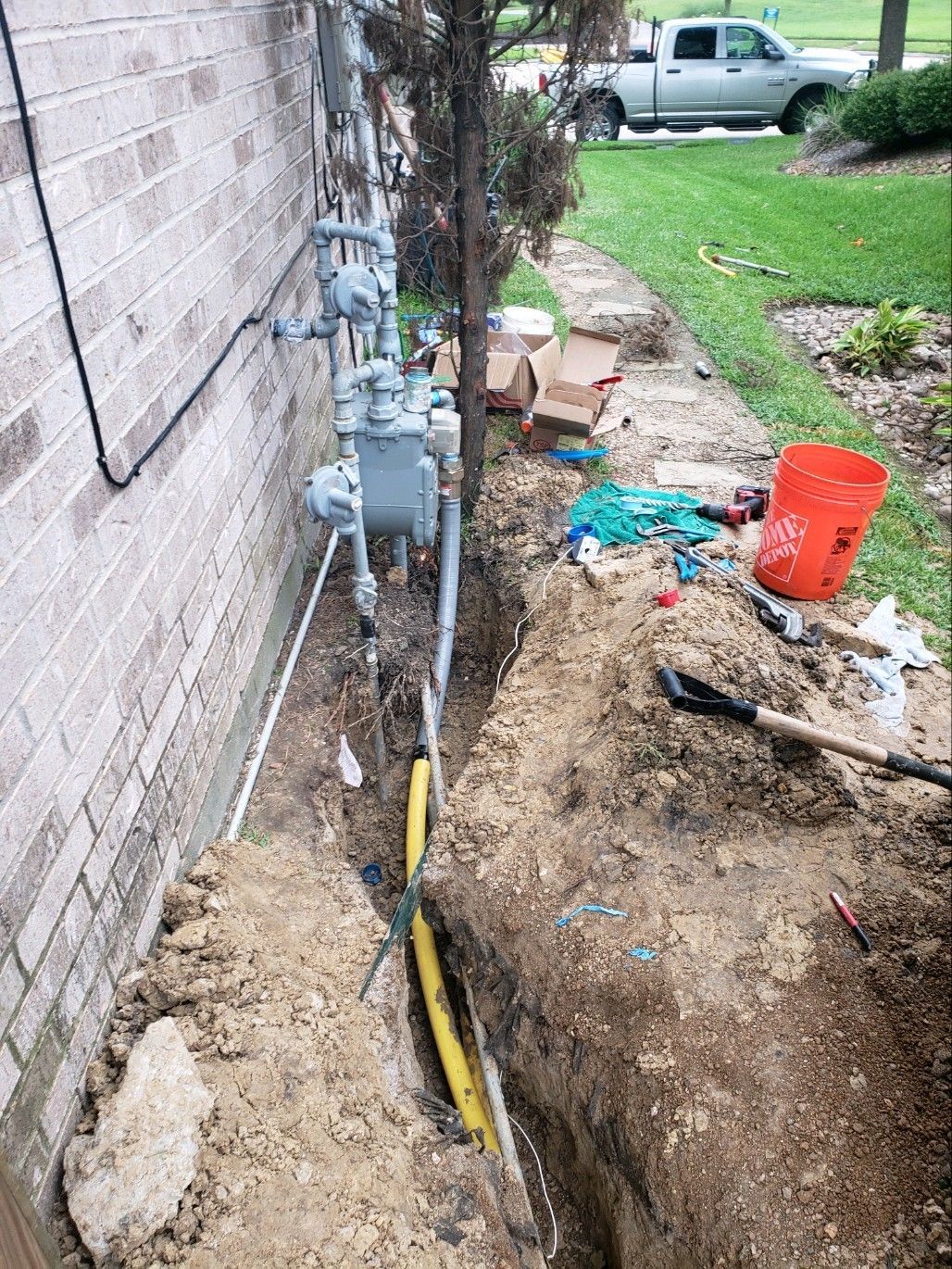 A hose is being installed in the dirt next to a brick wall.