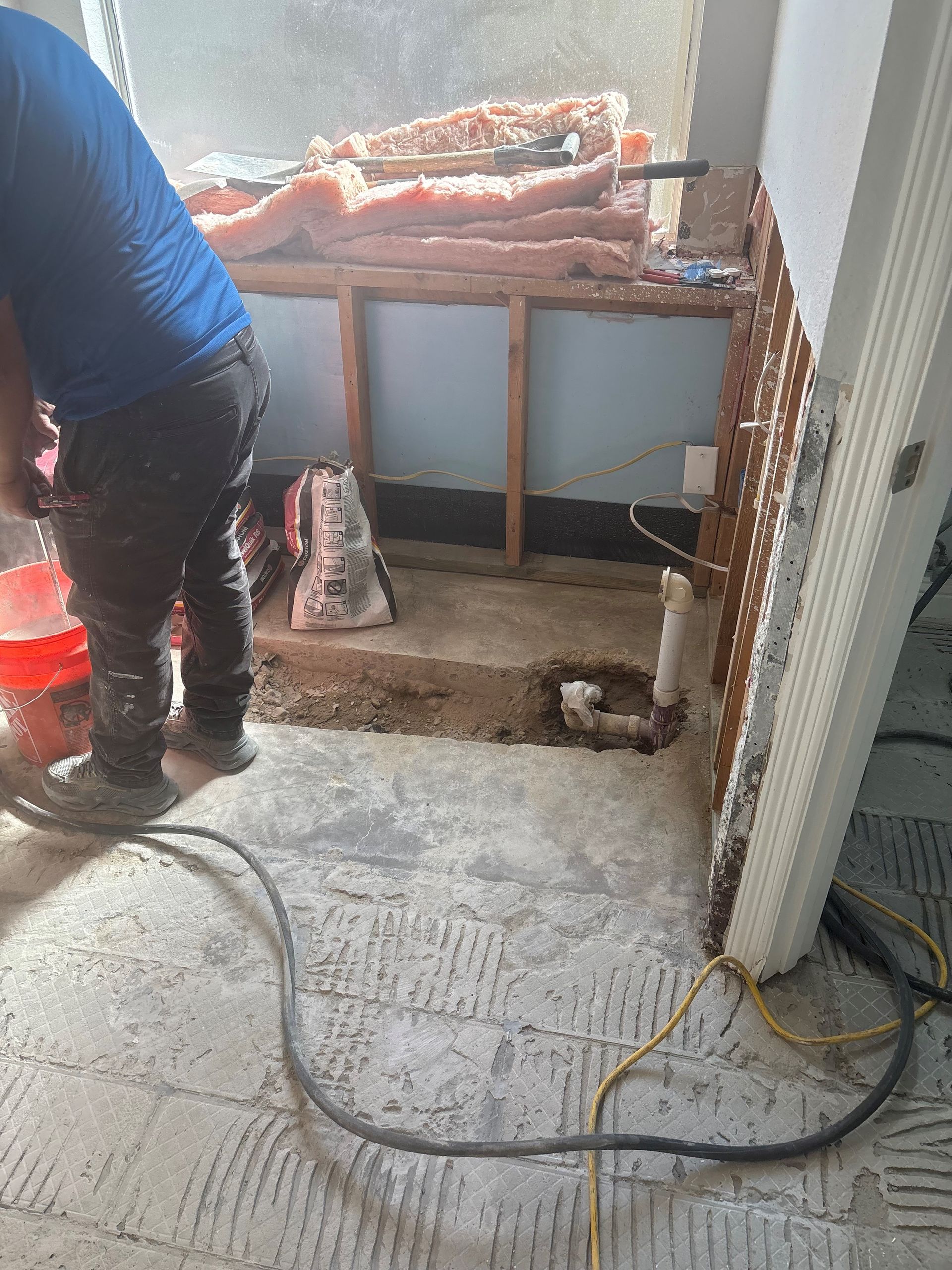 A man is working on the floor of a bathroom.