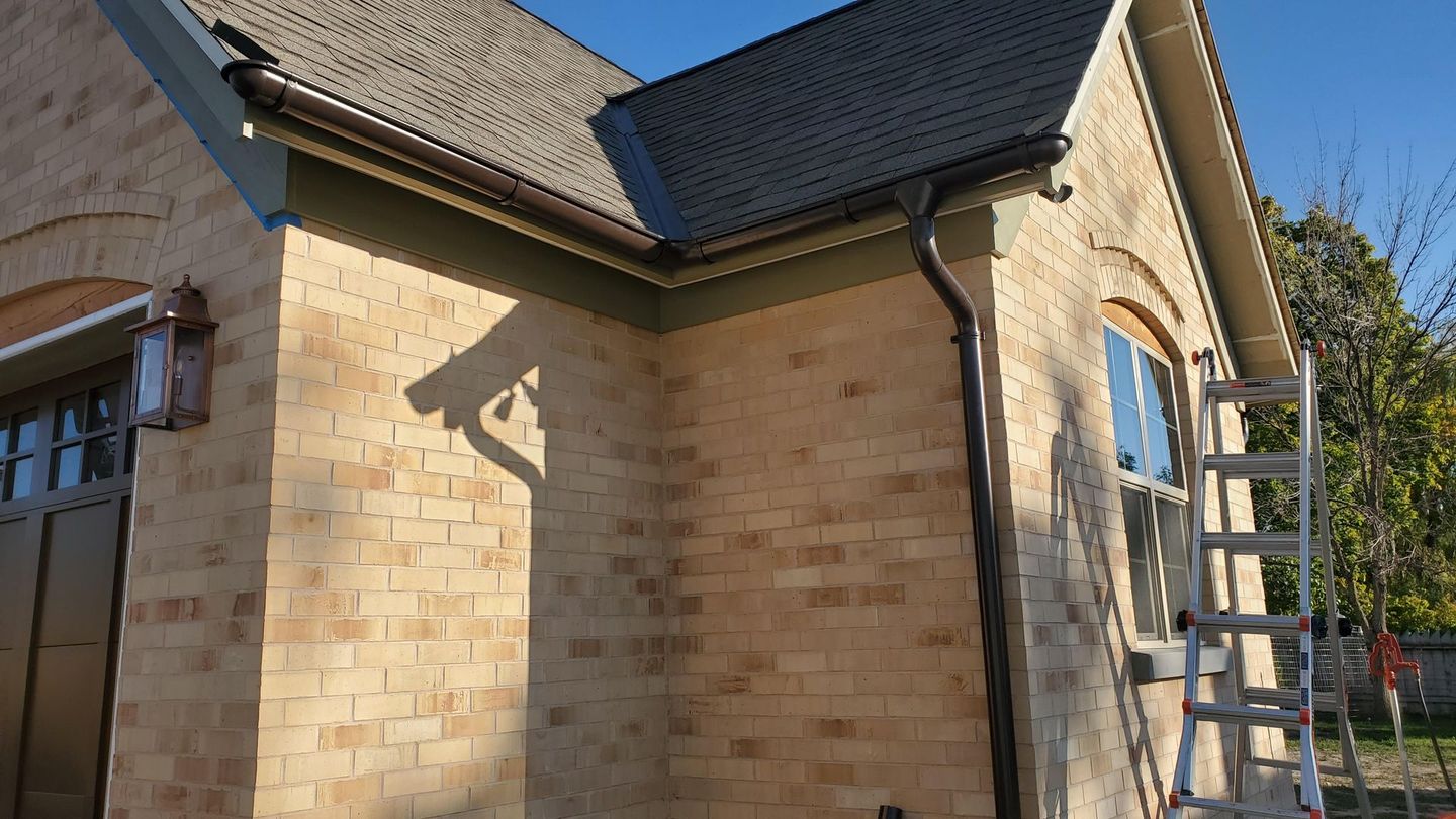 a man is standing on a ladder installing a gutter on a roof .