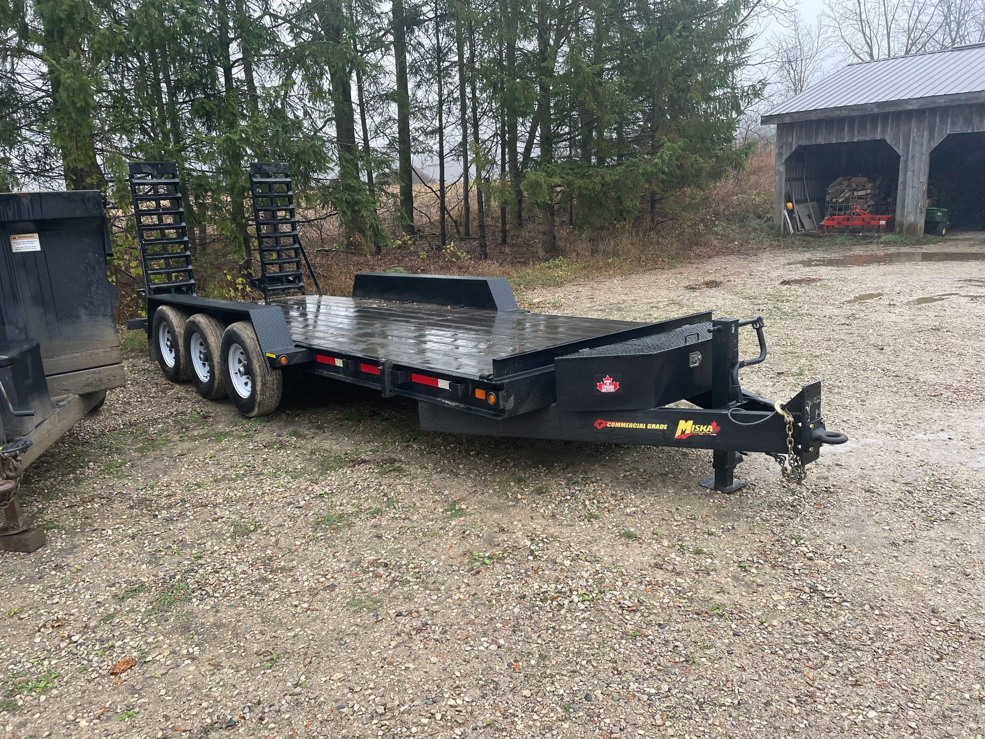A flatbed trailer is parked in a gravel lot next to a dumpster.