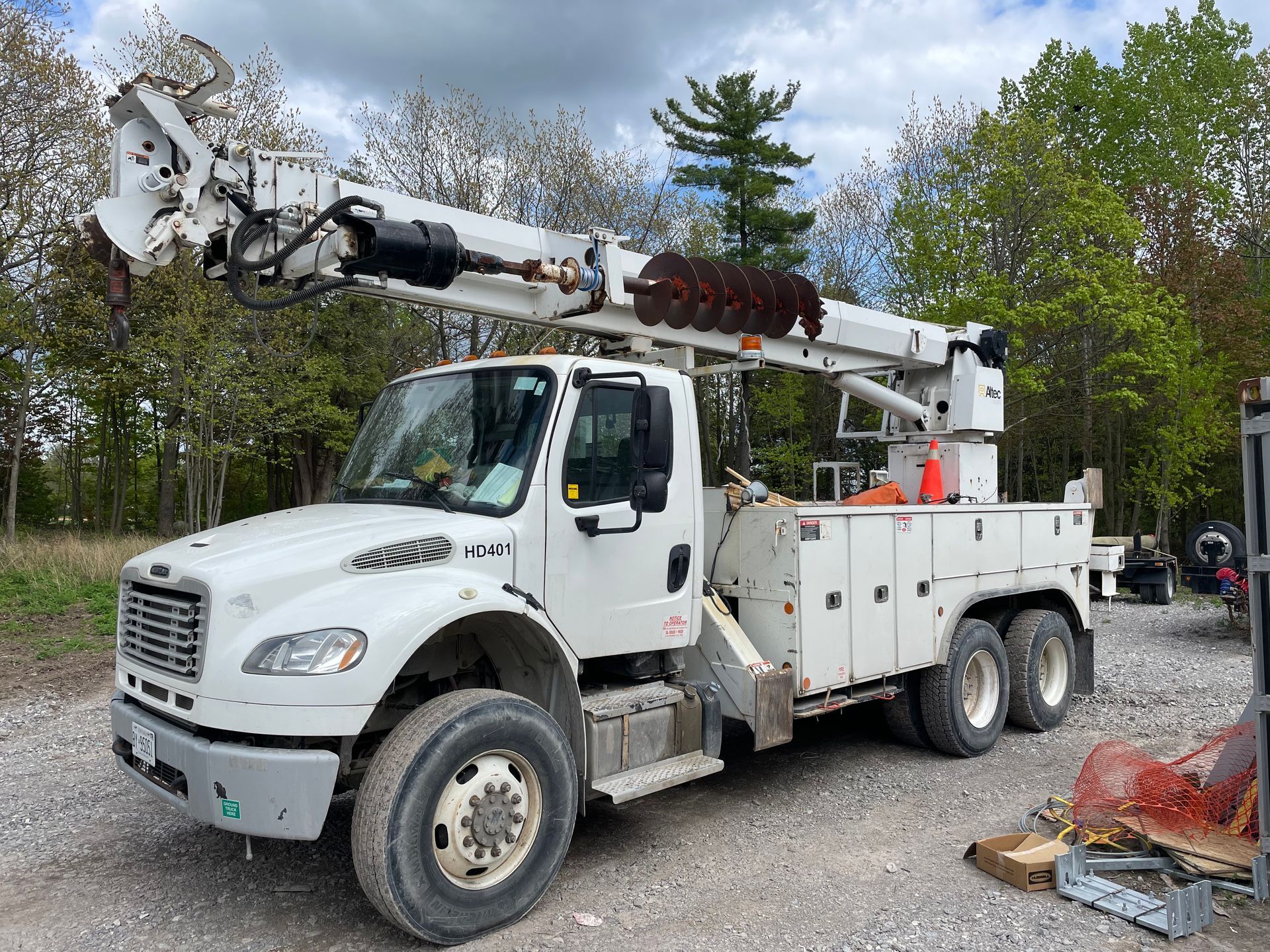 A white truck with a crane on top of it is parked in a gravel lot.