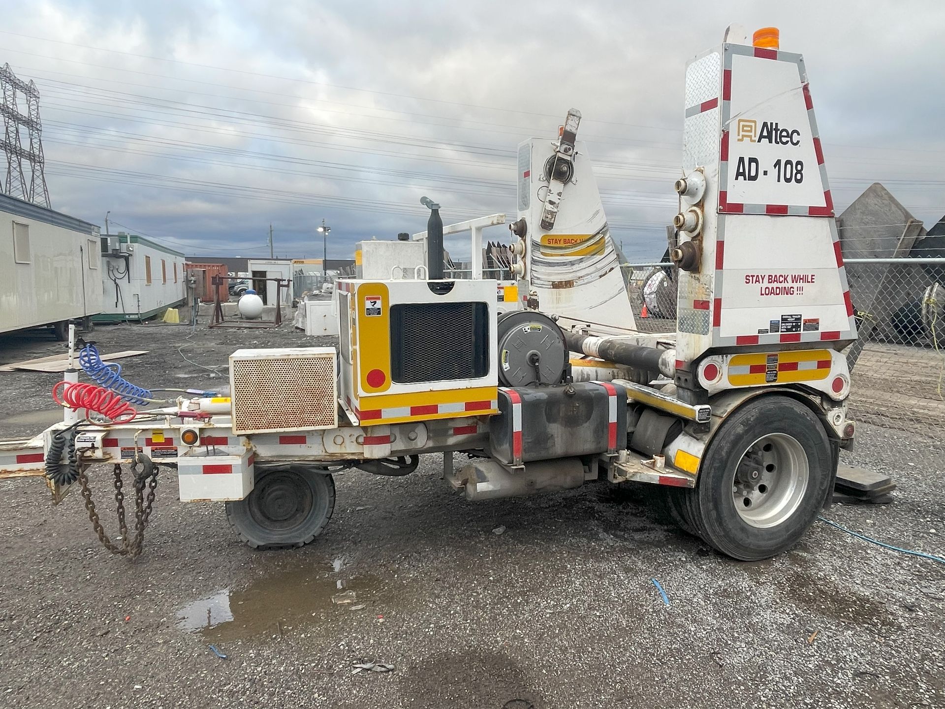 A white truck with a trailer attached to it is parked in a gravel lot.