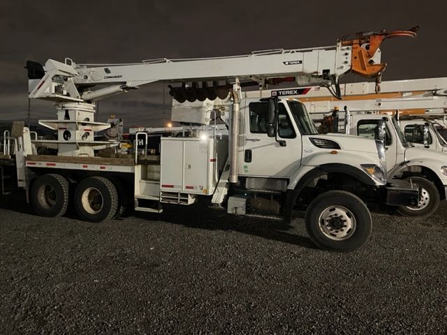 A row of utility trucks are parked in a gravel lot at night.