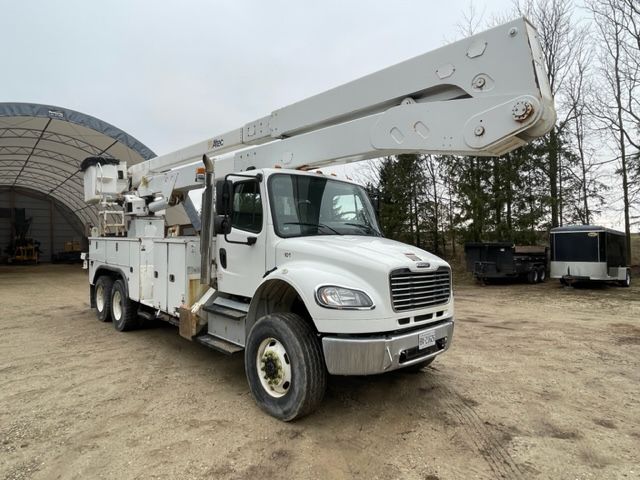 A white truck with a crane on top of it is parked in a dirt lot.