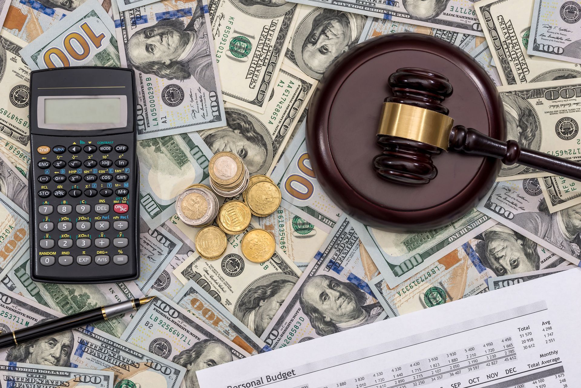 Calculator, gavel, coins, and pen on a background of American currency, suggesting financial or legal context.