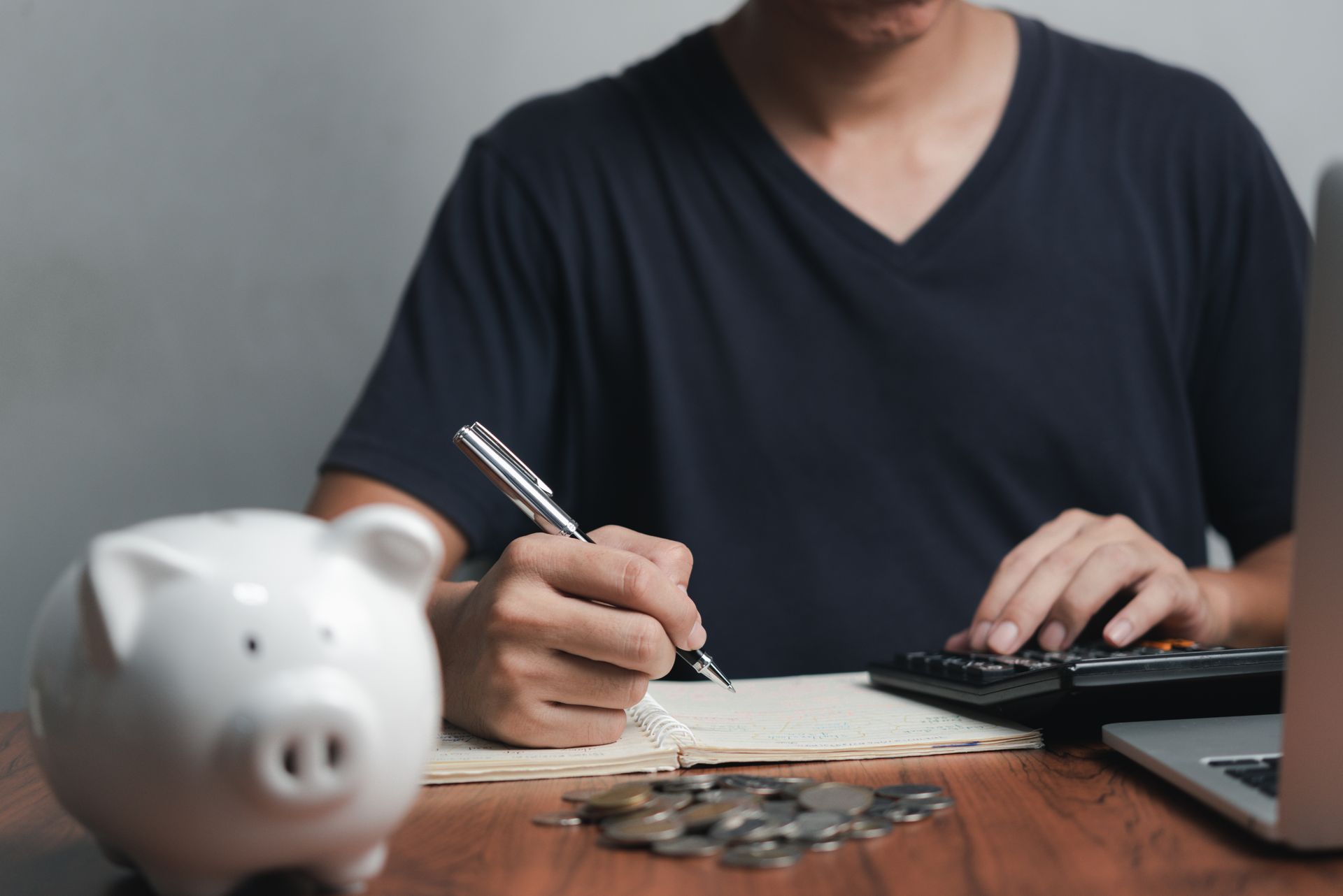 A man is sitting at a table with a piggy bank and a calculator.