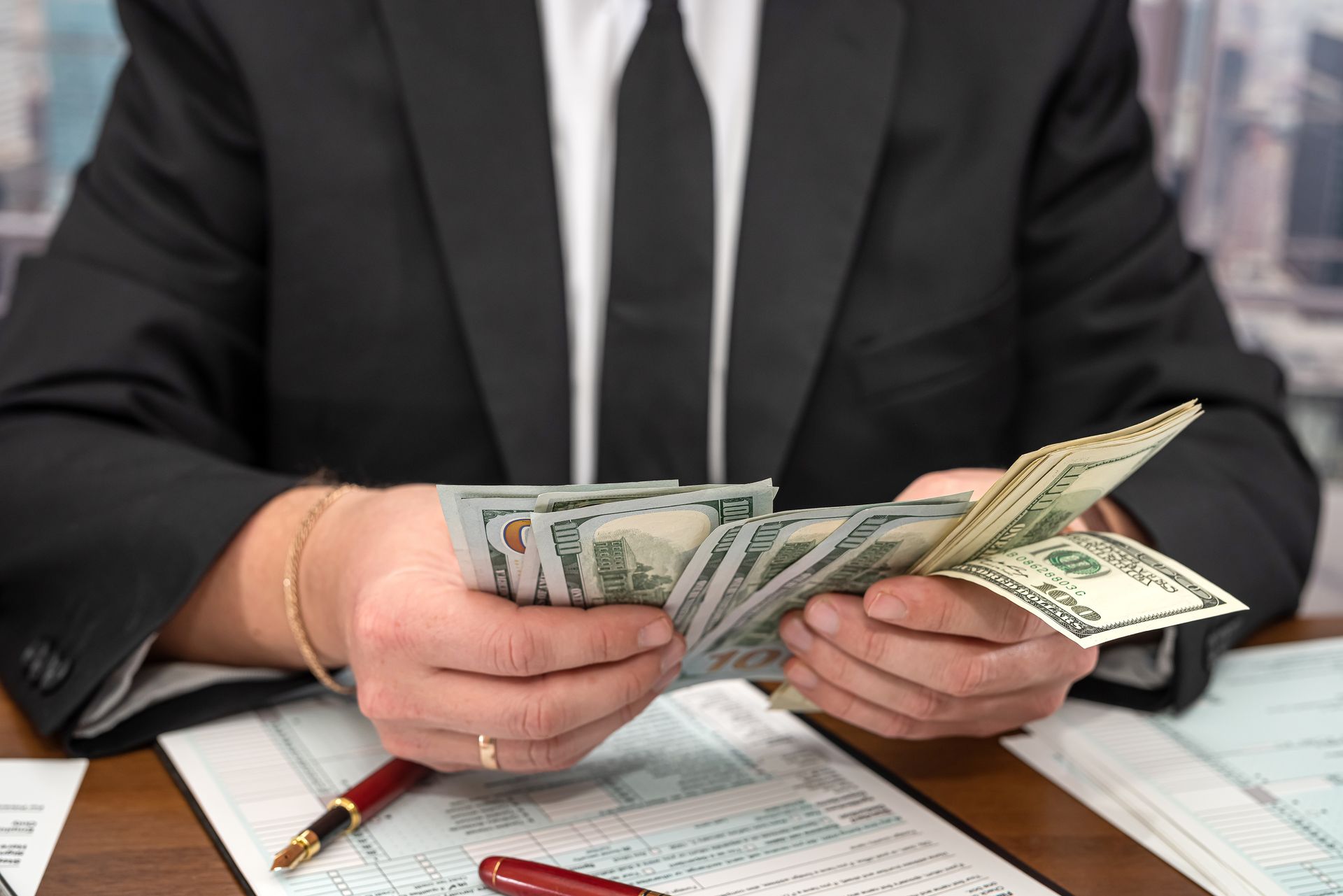 Man in suit counting a stack of US hundred-dollar bills.