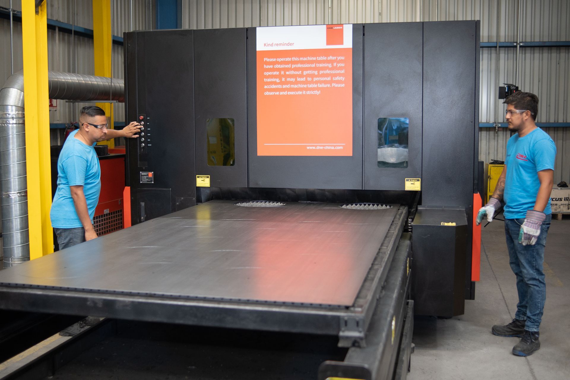 Dos hombres están parados junto a una gran máquina en una fábrica.