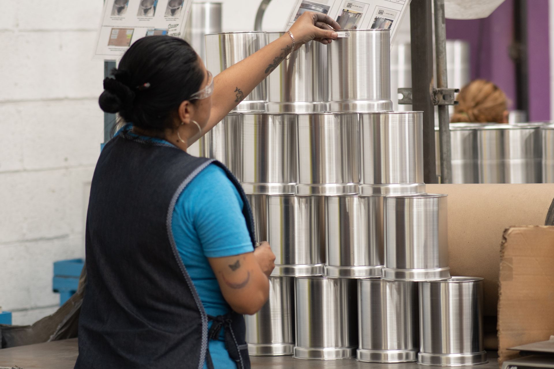 Una mujer está parada frente a una pila de piezas de acero inoxidable.