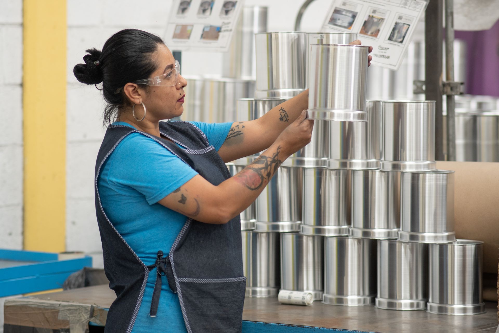 Una mujer está parada frente a una pila de piezasde metal en una fábrica.