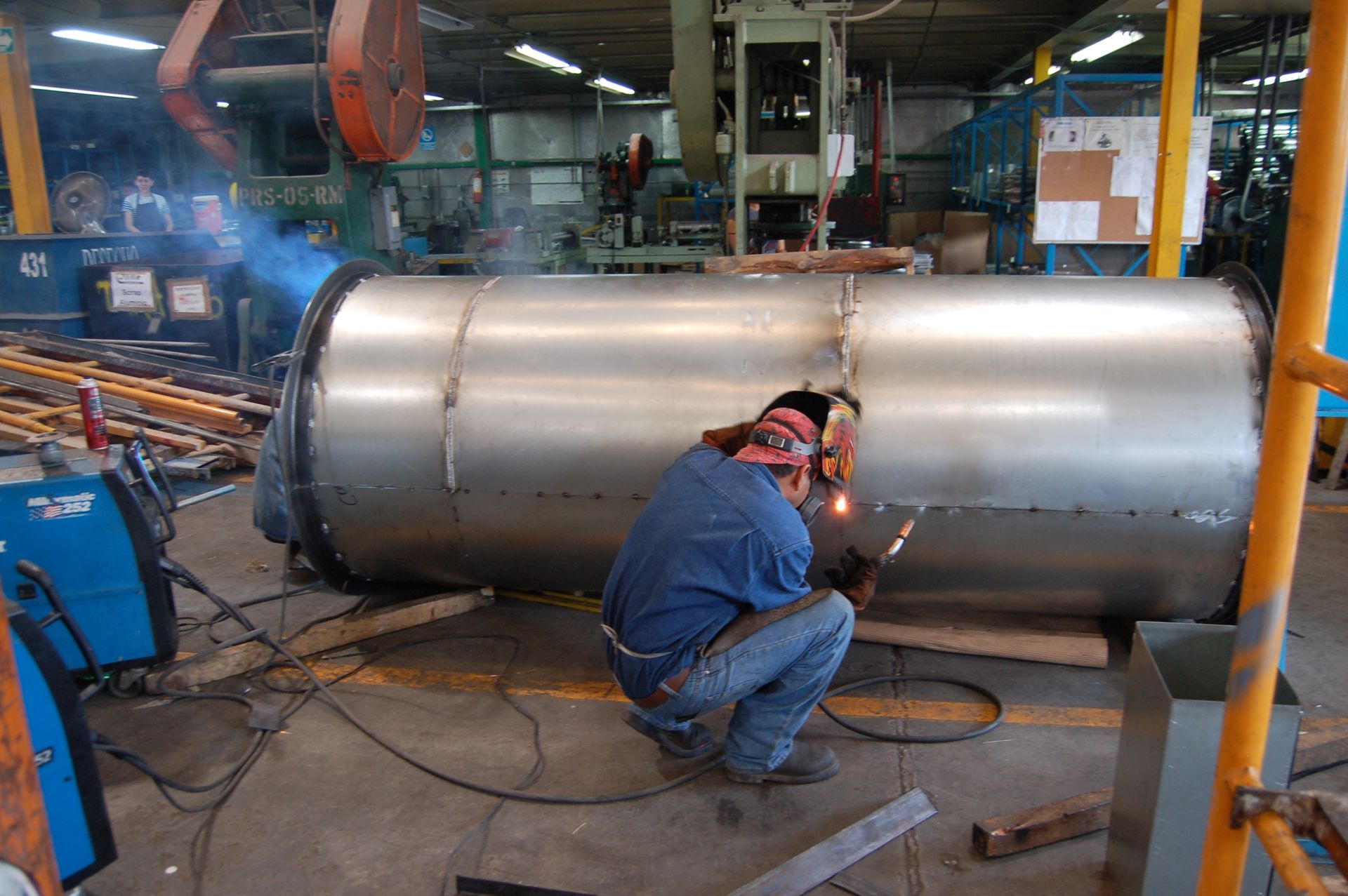 un hombre está soldando un gran tubo metálico en una fábrica.