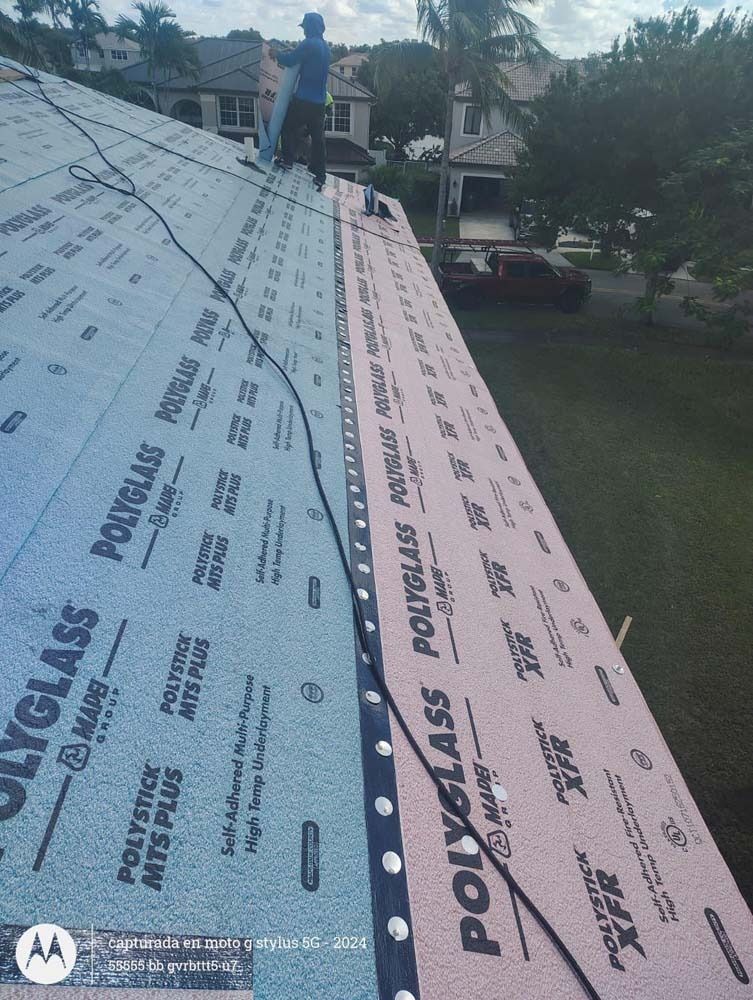 A worker installs blue and pink Polyglass underlayment on a slanted residential roof.