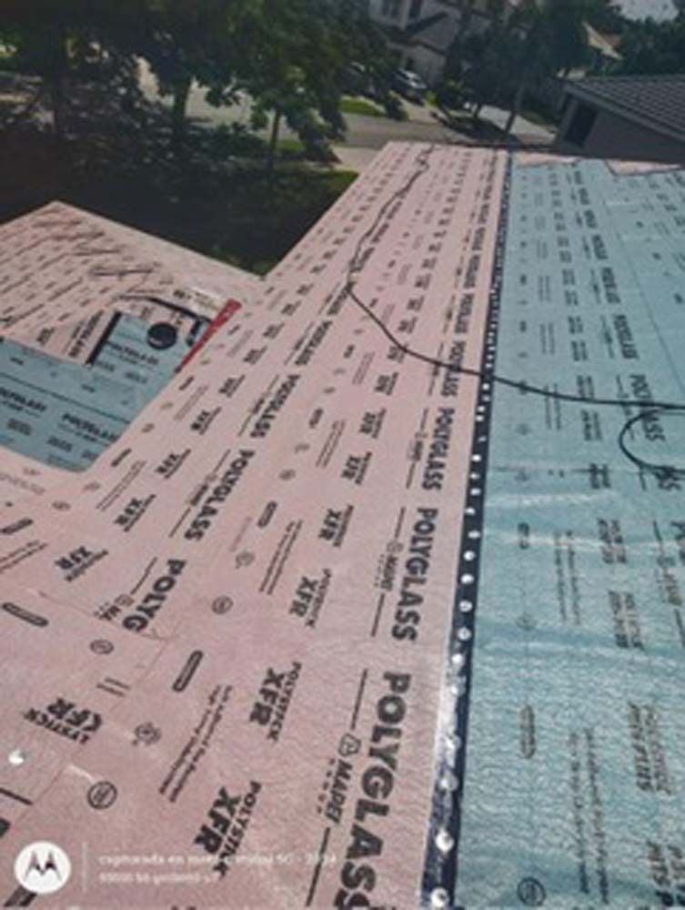 Roof underlayment being installed on a sloped residential roof, showing pink and blue Polyglass material sections.