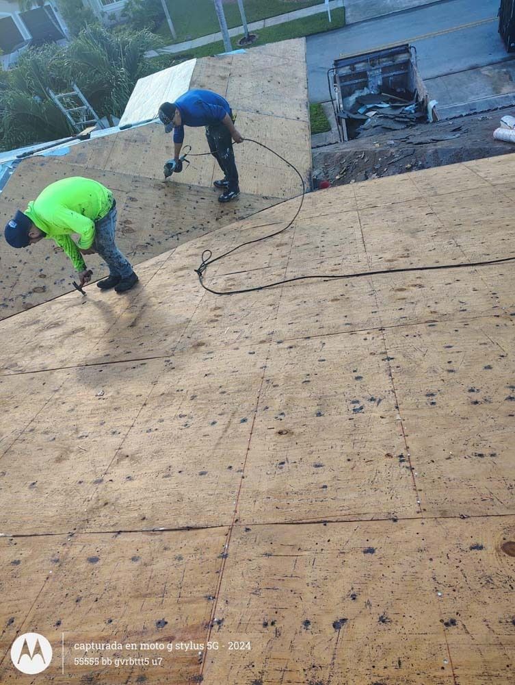 Two workers in high-visibility gear install plywood panels on a residential roof.