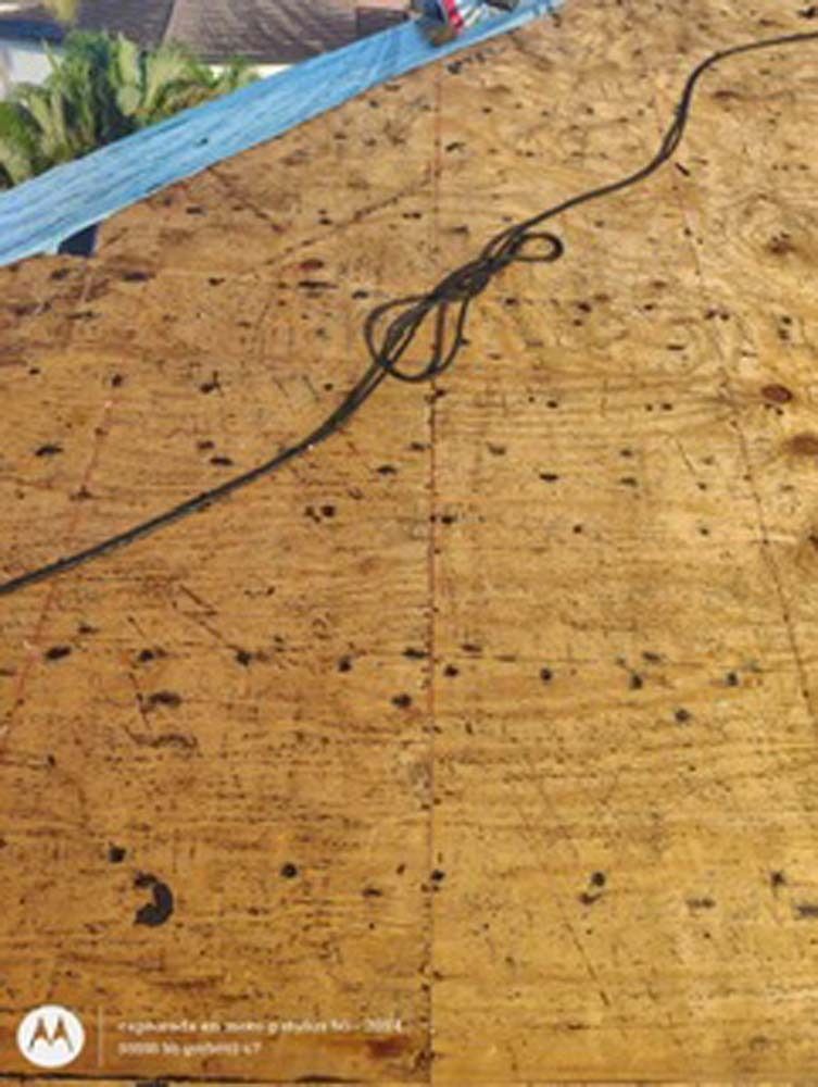 A black rope with a knot lies on top of a sheet of light-brown oriented strand board (OSB) under construction.