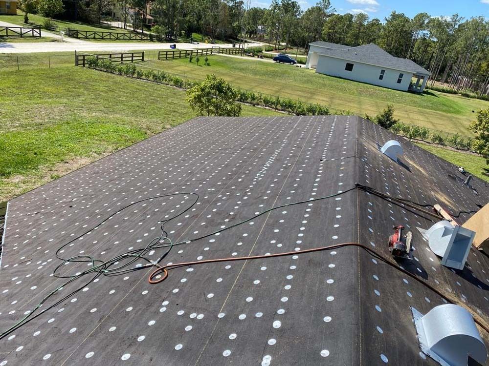 A sloped roof covered in black underlayment with white circular fasteners, featuring a safety rope and several metal vents.