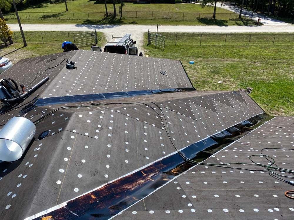 High-angle view of a residential roof undergoing construction, covered in black underlayment with evenly spaced fasteners.