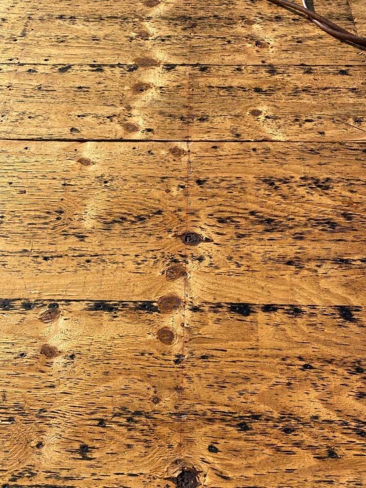 A close-up view of weathered, honey-colored wood floorboards featuring prominent grain patterns, dark knots, and texture.