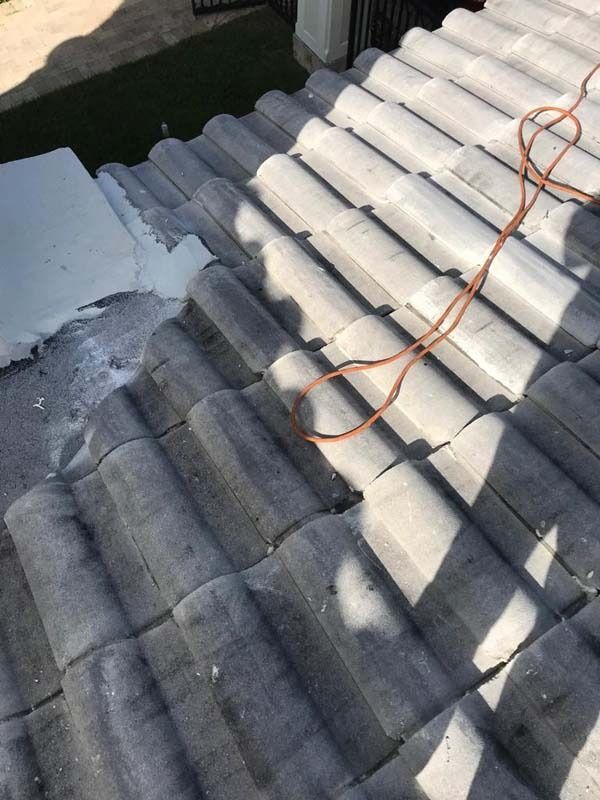 An orange extension cord coiled on gray roof tiles near a white painted section of a roof edge.