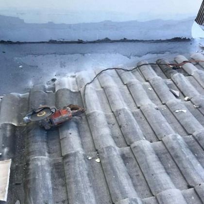 An orange power saw sits on a gray tiled roof next to a wall with a fresh layer of waterproof sealant.