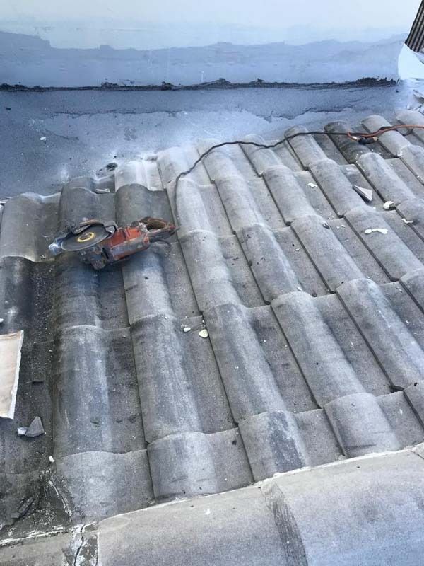 A power saw sits on a sloped roof with grey concrete tiles next to a freshly sealed joint.