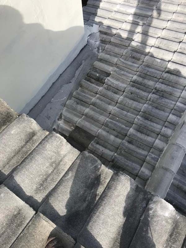 A high-angle view of a tiled roof, showing the junction between a wall and the roof tiles with grey flashing material.