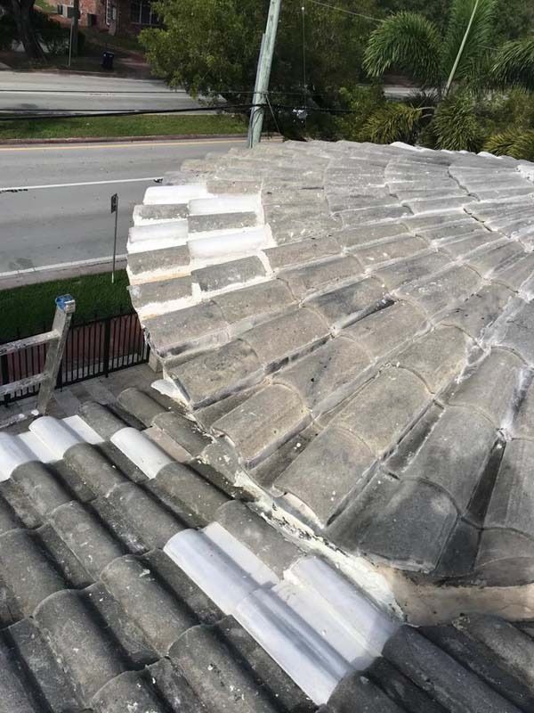 A high-angle view of a grey concrete tile roof showing a curved transition area being repaired with white sealant.