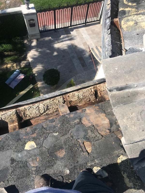 A first-person view looking down from a residential roof onto a paved driveway and gated yard during a repair project.