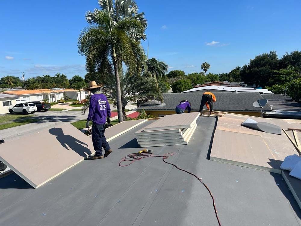 Three construction workers installing insulation boards on a residential flat roof on a sunny day.