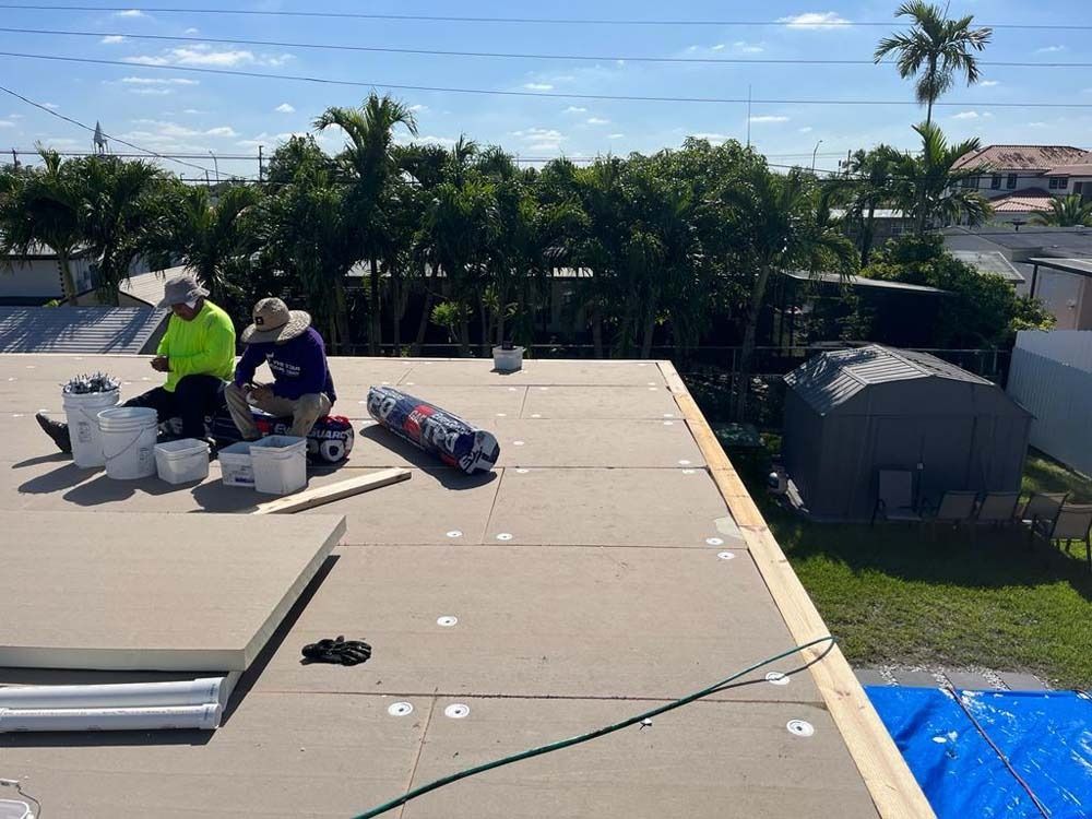 Two construction workers in hats install insulation panels on a flat rooftop on a sunny day.