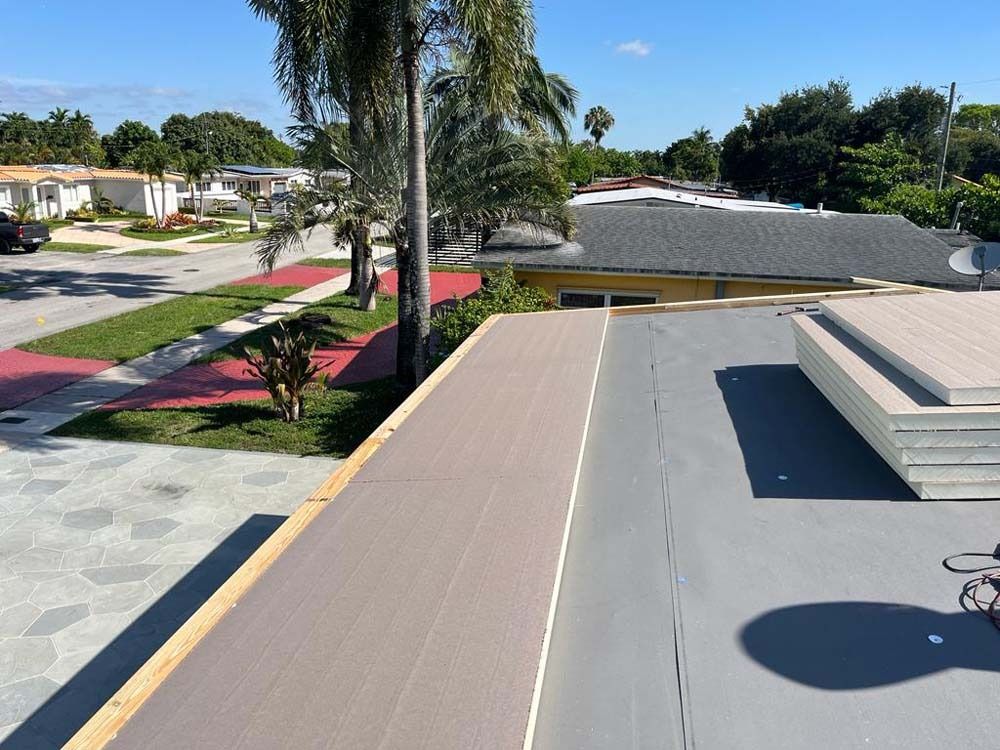 View from a flat roof showing a newly installed brown surface next to a grey section, overlooking a suburban street.