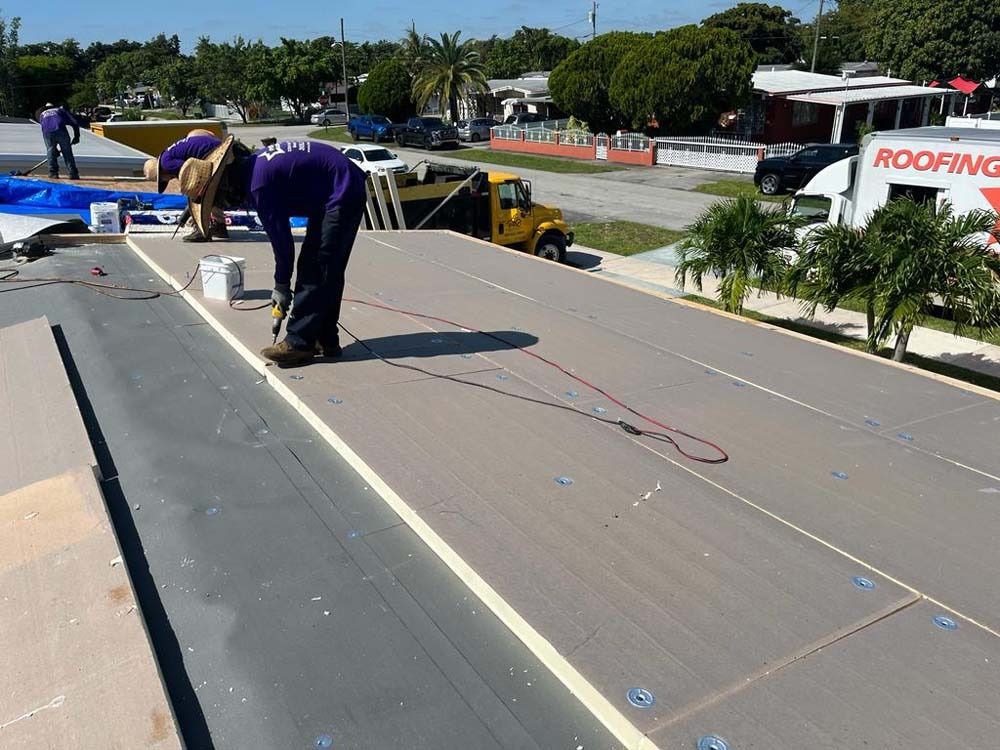 Workers in purple shirts install insulation boards on a flat residential roof on a sunny day.