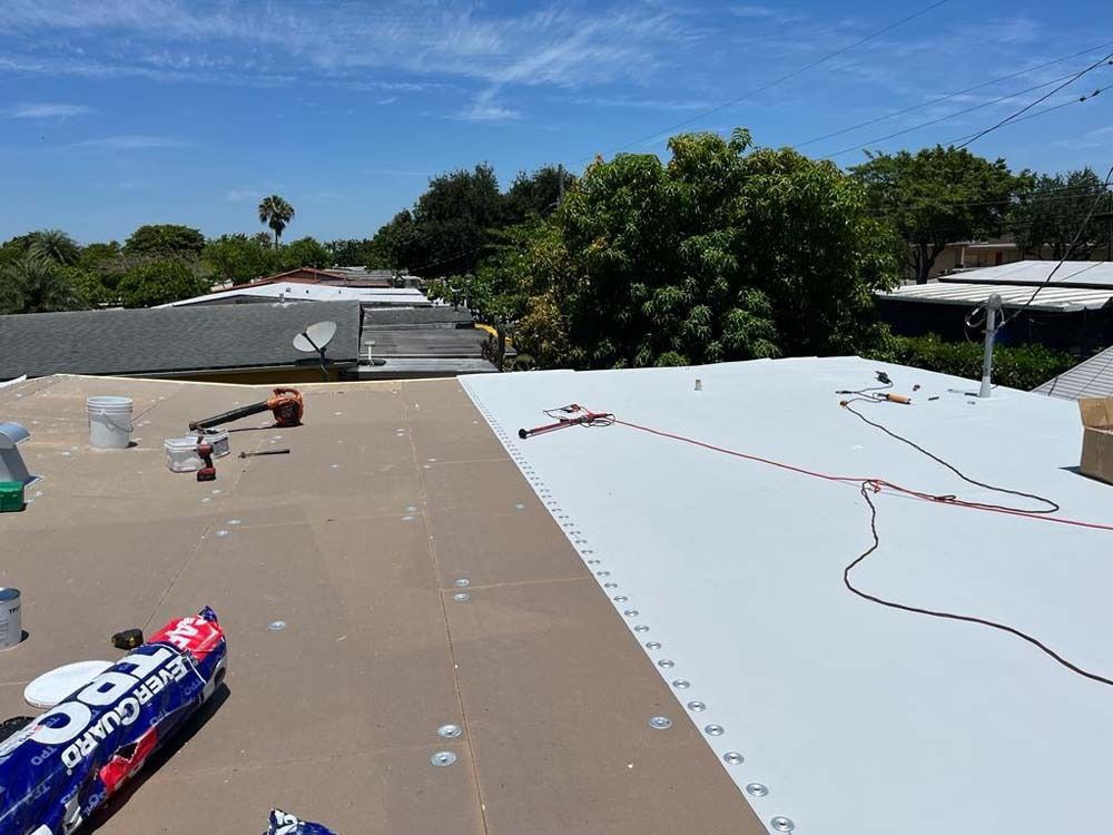 A construction worker installs white TPO roofing membrane over insulation boards on a residential roof on a sunny day.