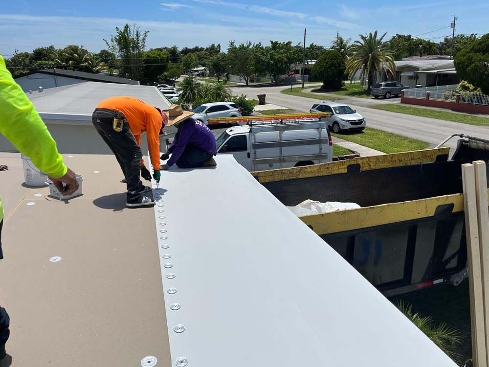 Two workers in high-visibility shirts install white roofing material on a residential roof near a dumpster.