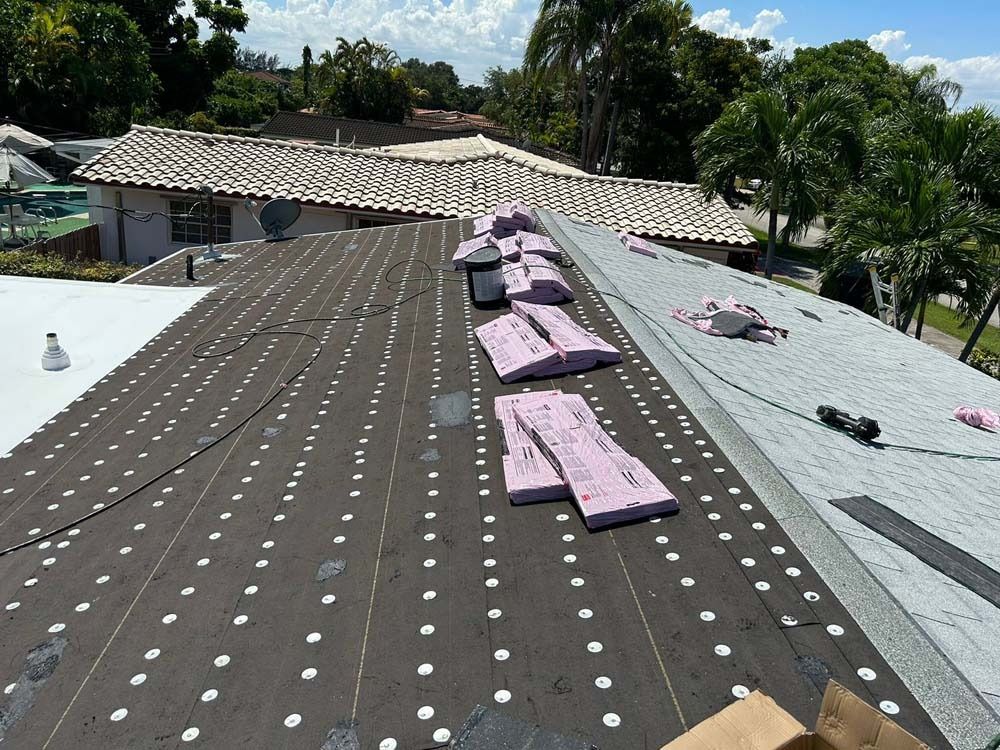 A residential roof under construction with dark underlayment, pink foam insulation boards, and gray shingles.