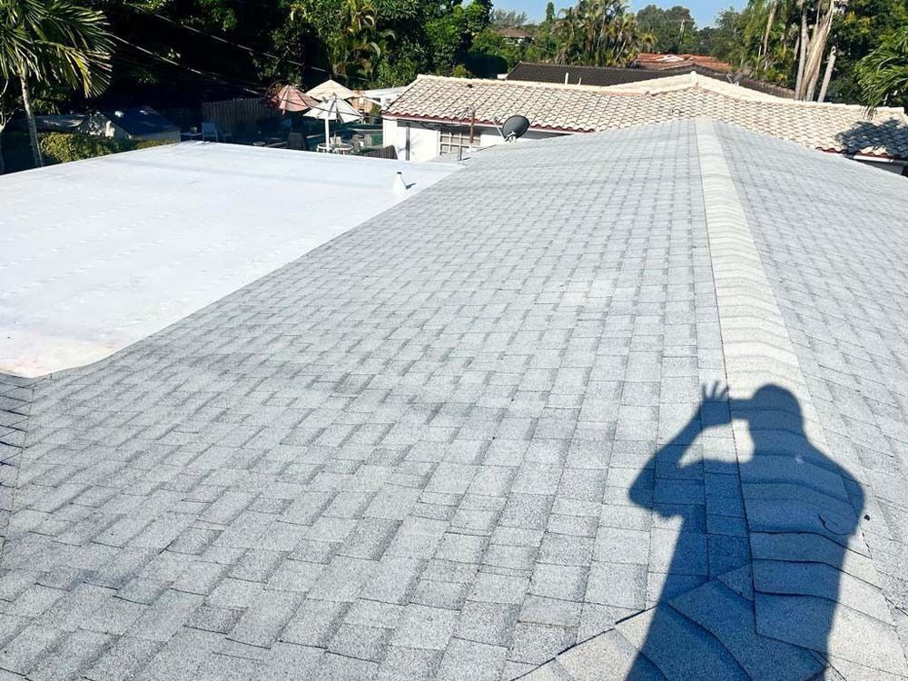 A gray shingled roof meets a flat, white section, with a person's shadow cast onto the shingles in the foreground.