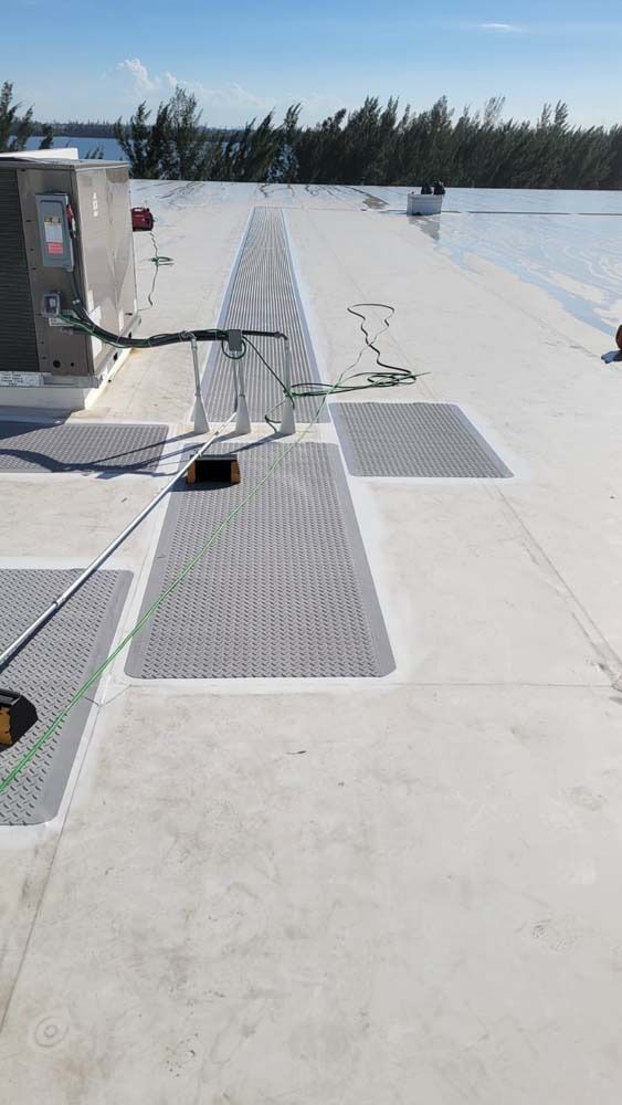 A flat commercial roof with grey walkway mats leading to HVAC equipment and a reflective triangular vent cover.