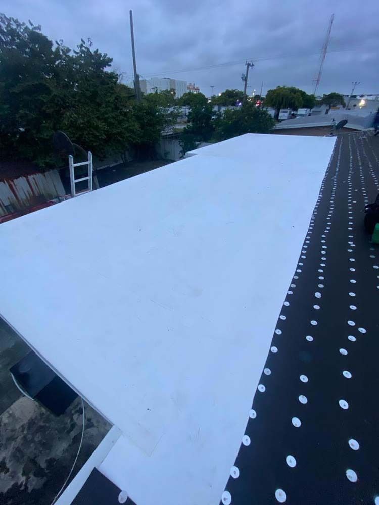 A partially installed white flat roof membrane over dark, dotted underlayment on a building exterior.