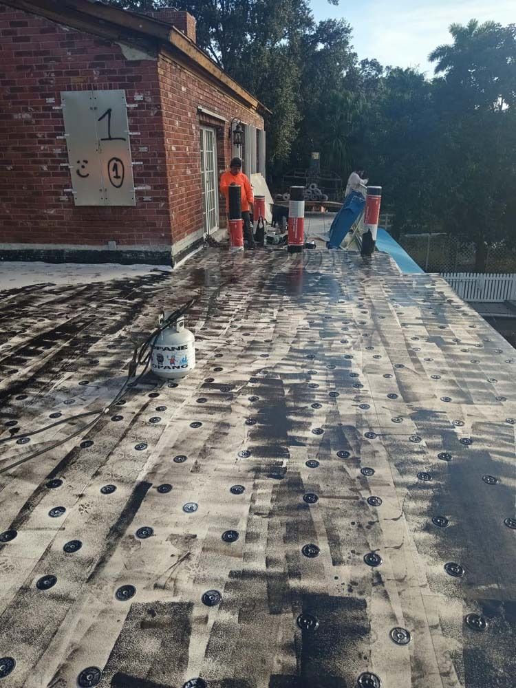 Roofers installing a membrane roof on a brick building, with a propane tank and fasteners visible on the deck.