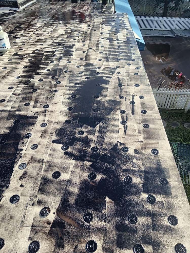 A low-angle view of a flat roof under construction, showing insulation boards secured with circular fasteners and adhesive.