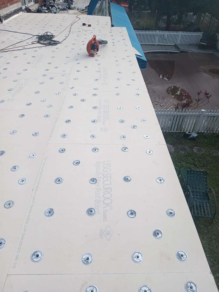 A rooftop covered in white insulation panels fastened with metal plates and screws, seen from a high angle.